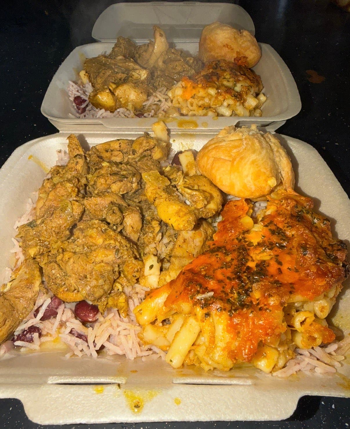 Two takeaway boxes of curry, rice and peas, mac and cheese and dumplings